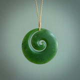 This picture shows a hand carved jade koru pendant. It is a deep green with orange colour and is a wonderful, large sized piece of jewellery. The cord is a four plait beige colour and adjustable so that you can position the pendant where it suits you best. This koru was carved for us by Ric Moor. Delivery is free worldwide.
