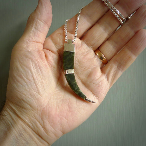 This picture shows a jade and sterling silver talon pendant with an adjustable cord. The pendant looks a little like a fang. A hand made unique and contemporary necklace hand carved here in New Zealand.