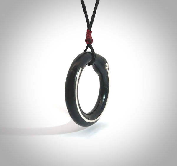 This picture shows a hand carved jade circle pendant with sterling silver inlay. The jade is a very dark green with a shimmer of black tones in the stone. It is suspended from an adjustable Black or Sage coloured cord. Delivery is free worldwide.