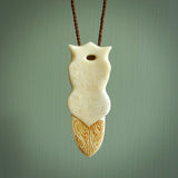 This is a large carved Koruru pendant. It is made from two materials - New Zealand Paua Shell and Bone. The face of the Koruru is carved with a traditional design in the front. It has a protruding tongue which is also carved and the back face has traditional carved designs. This is a large and very traditional pendant that is a collectors piece. This piece is provided on a brown adjustable cord.