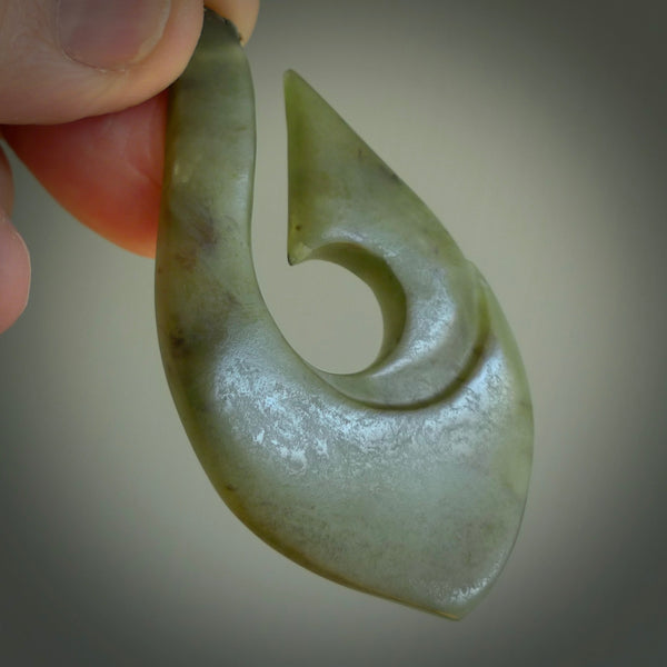 A hand carved hook design pendant, carved in New Zealand Jade. The colour is a beautiful green. The cord is green and tan and is length adjustable. Hand made by Rueben Tipene. Delivered with Express courier in a woven kete pouch.