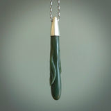 This picture shows a hand carved Inanga Pounamu, jade drop pendant with sterling silver cap and chain. The jade is a very dark green with a shimmer of light blue tones in the stone. It is suspended from a sterling silver clasp and we supply a sterling silver chain. Delivery is free worldwide.