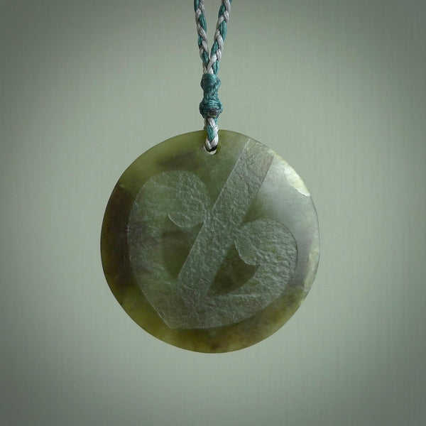 Hand carved jade disc pendant. One side has a double koru etched into the face. This is a subtle and beautiful design. The other side is plain. The cord is a tan colour and is adjustable. The piece was carved for NZ Pacific by Rueben Tipene.