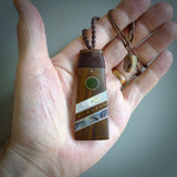 This photo shows a medium sized Toki pendant hand carved from lignum vitae with New Zealand Pounamu Jade, Mother of Pearl and Paua Shell inlay alongside; brass and silver. This is a stand out one off necklace for those who appreciate art to wear. It is provided with a cord in brown that is a fixed length with Paua Shell Toggle. We ship this piece worldwide and shipping is included in the price.