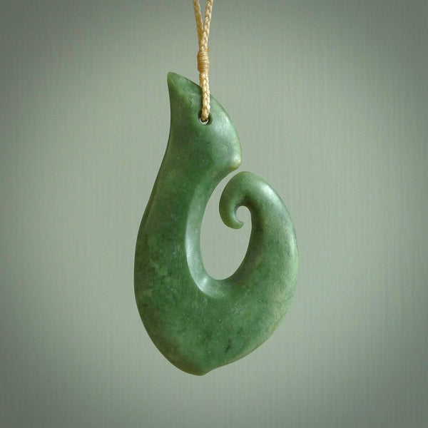 This picture shows a hand carved jade koru pendant. It is a deep green colour and is a wonderful, large sized piece of jewellery. The cord is a four plait beige colour and adjustable so that you can position the pendant where it suits you best. This koru was carved for us by Ric Moor. Delivery is free worldwide.