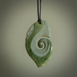 This photo shows a koru with a face carved into the leading edge. The artist, Kerry Thompson, has carved this beautifully and he has polished parts of the carving to a high shine, and other parts he has left in a matte finish. The contrast is beautiful. The pendant is suspended from a plaited black cord which is adjustable.