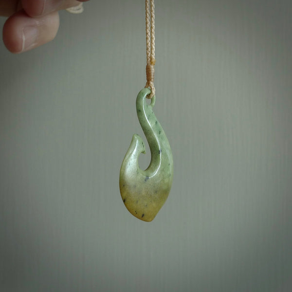 This picture shows a jade hook pendant, also called a hei-matau, carved for us in New Zealand jade. The jade is a wonderful deep mint green pounamu. This is a rare jade loved and valued for its distinctive colour. The carver is Ric Moor - and this is a beautiful example of his work. The cord is a four-plait, adjustable brown coloured necklace.
