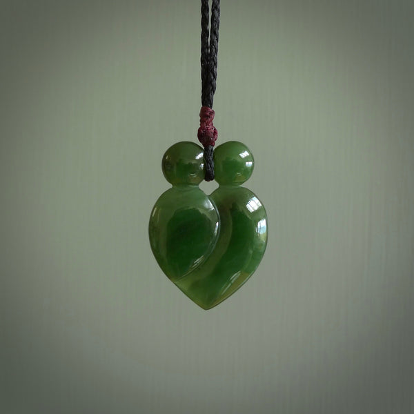 This picture shows a stylised couple in a close embrace sharing a kiss. The pendant is hand carved from a bright tree, faultless piece of British Columbian jade. The cord is a 3-ply plaited black with a plum coloured floret.
