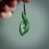 This picture shows a jade hook pendant, also called a hei-matau, carved for us in New Zealand jade. The carver is Ric Moor - and this is a beautiful example of his work. The cord is a four-plait, adjustable brown coloured necklace.
