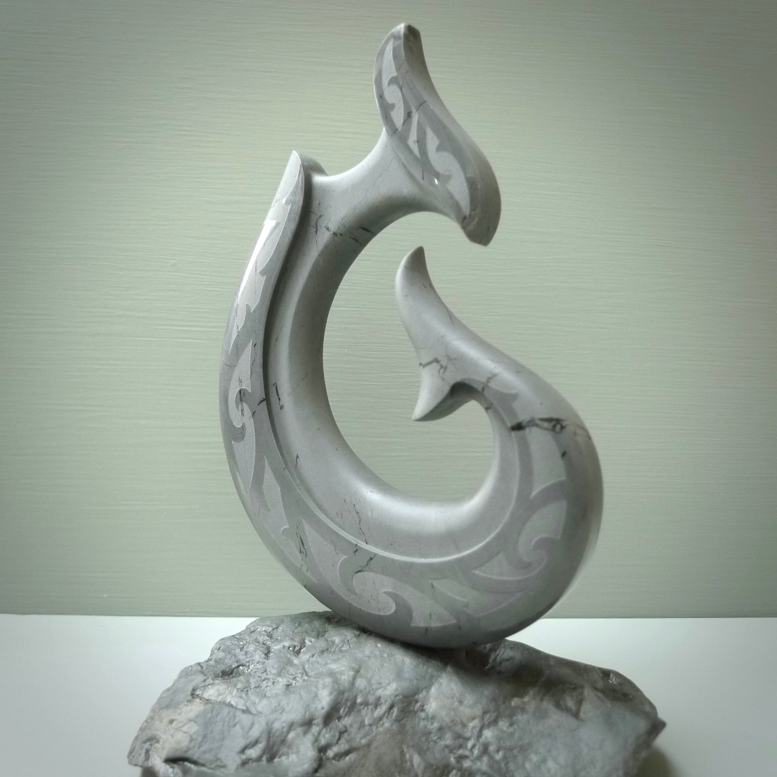 Hand carved large New Zealand Argillite Stone Matau, hook carving displayed in a New Zealand Pākohe stand sculpture. Hand carved here in New Zealand by Kerry Thompson. This is a 'one only' sculpture, a beautiful display piece.