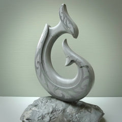 Hand carved large New Zealand Argillite Stone Matau, hook carving displayed in a New Zealand Pākohe stand sculpture. Hand carved here in New Zealand by Kerry Thompson. This is a 'one only' sculpture, a beautiful display piece.