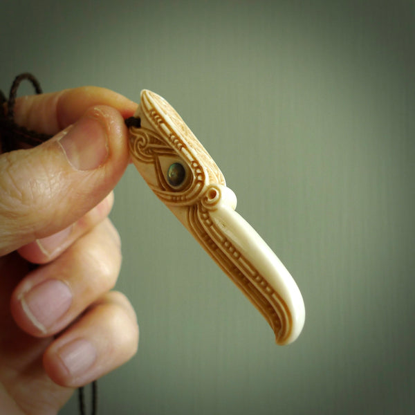 This picture shows a carved kāhu, hawk in bone. It is a drop shaped pendant. The artist has carved traditional decorative kowhaiwhai designs into the body and these run up the sides of the hawk. These have specific meanings. It is provided with a hand-plaited brown cord that is length adjustable. Shipping is included and we ship worldwide.