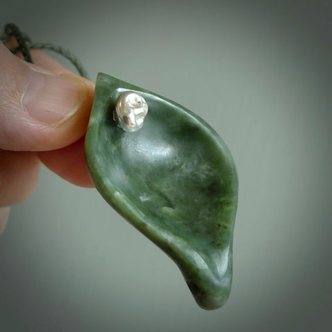 This picture shows a hand carved drop pendant made from a deep green coloured New Zealand Pounamu, jade. The front face is a concave, cupped design and the back is round. It is provided with an adjustable fern green cord in a woven kete pouch. Shipped to you with Express Courier.