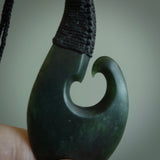 This picture shows a large deep green large jade hook pendant, also called a hei-matau, carved for us in New Zealand jade. The carver is Donna Summers - and this is a beautiful example of his work. The cord is a four-plait, adjustable black coloured necklace. 