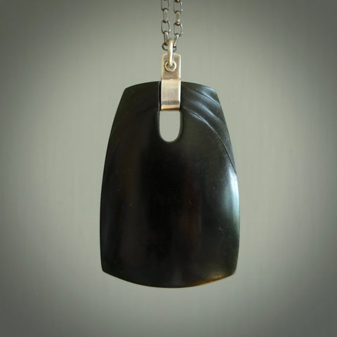 This photo shows a square drop pendant suspended from a silver clasp and silver chain. The jade is a deep, dark New Zealand jade with a subtle dual wave design on the front. A lovely soft New Zealand jade pendant carved for us by Josey Coyle.