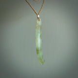 This picture shows a hand carved Spoon River White Jade drop pendant with adjustable cord. The jade is a very light, white green with a shimmer of darker tones in the stone. It is suspended from a tan coloured cord. Delivery is free worldwide.