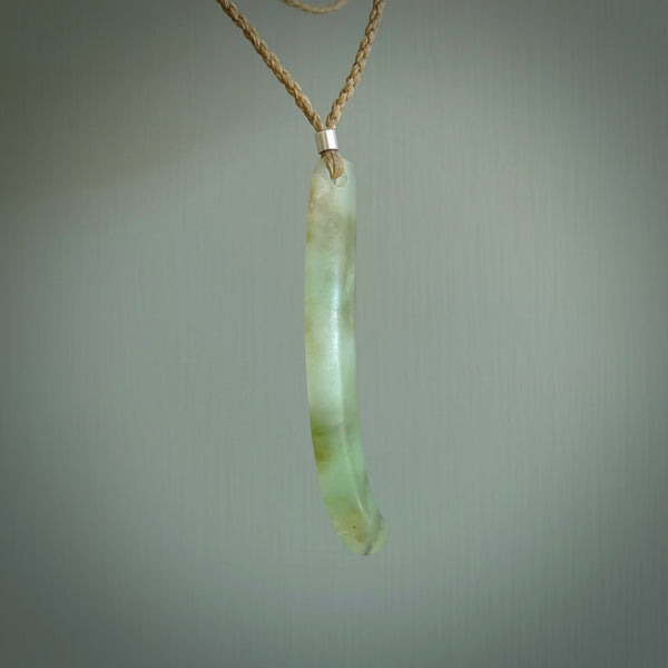 This picture shows a hand carved Spoon River White Jade drop pendant with adjustable cord. The jade is a very light, white green with a shimmer of darker tones in the stone. It is suspended from a tan coloured cord. Delivery is free worldwide.