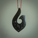 A hand carved large New Zealand Jade Hook, Matau, necklace. The cord is a Passion and Juicy Red colour and is length adjustable. A large sized hand made hook necklace by New Zealand artist Rueben Tipene. One off work of art to wear.