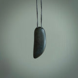 Greywacke Beach Stone drop, pendant hand made here in New Zealand. Hand carved by Rhys Hall for NZ Pacific. Handmade jewellery for sale online. The cord is grey and has a loop and pebble toggle closure. Unique necklace for men and women. Drop necklace hand made from New Zealand Greywacke Beach Stone.