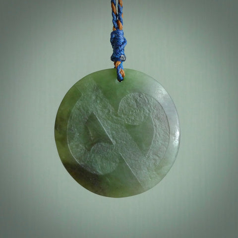 Hand carved jade disc pendant. One side has a double koru etched into the face. This is a subtle and beautiful design. The other side is plain. The cord is a tan colour and is adjustable. The piece was carved for NZ Pacific by Rueben Tipene.