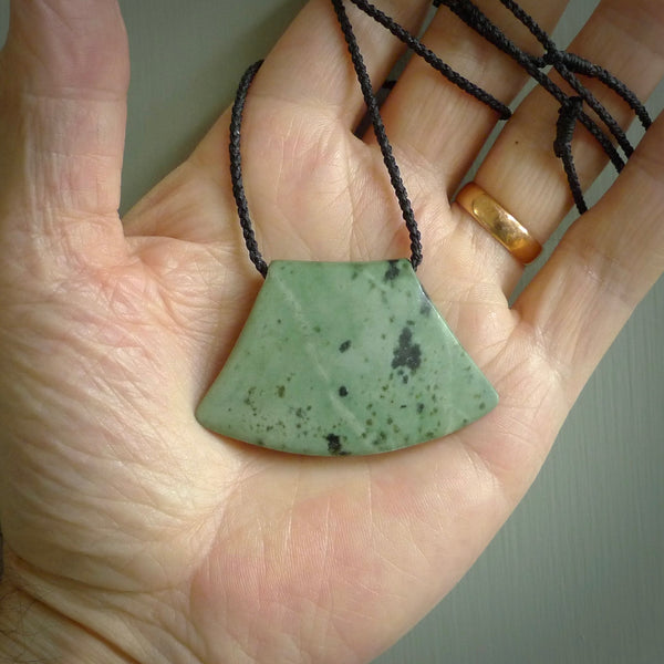 This picture shows a hand carved jade contemporary half-shield pendant. It is a mint green colour. This is a wonderful piece of jewellery. The cord is hand plaited and adjustable so that you can position the pendant where it suits you best. This piece was carved for us by Ric Moor. Delivery is free worldwide.