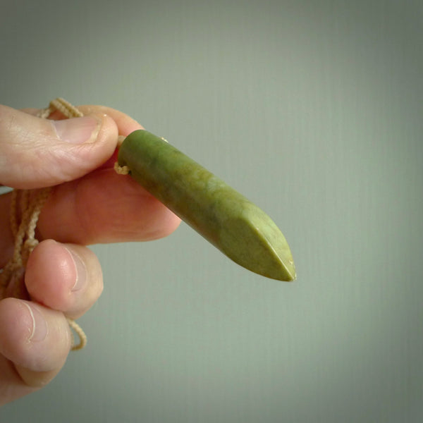 This picture shows a hand carved flower jade drop pendant by Ric Moor. The jade is a wonderful green with a shimmer of orange tones in the stone. It is suspended from a beige adjustable cord. Delivery is free worldwide.