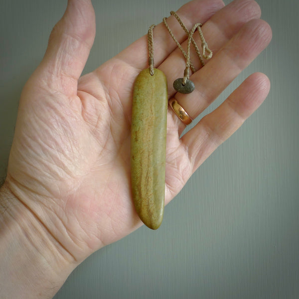 Raukaraka Pounamu drop pendant. Hand carved by Rhys Hall for NZ Pacific. Handmade jewellery for sale online. The cord is a 4-braid plait in tan and has a loop and pebble toggle closure. Drop necklace for men and women. Scandinesian Toki necklace hand made from New Zealand Jade.