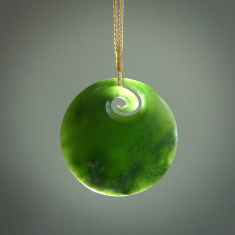 This picture shows a large hand carved jade koru pendant. It is a darker green colour which is quite translucent where the jade is thin. Although a large piece, it is a wonderful, delicate piece of jewellery. The cord is hand plaited and adjustable so that you can position the pendant where it suits you best. This koru was carved for us by Ric Moor. Delivery is free worldwide.