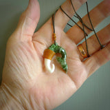 This photo shows a beautiful jade whaletail with bone pendant. It is handcarved from a piece of mottled green Jade, with fascinating mauve tinges through the stone. We have this on a burnt gold and flax coloured, adjustable cord with a burnt gold green floret just above the pendant and binding. We ship this worldwide with an express courier service. Postage is free.