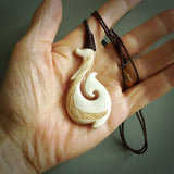 This picture shows a carved hook in bone. The artist has carved traditional decorative kowhaiwhai designs into the body and these run up the insides of the matau. These have specific meanings. It is provided with a hand-plaited brown cord that is length adjustable. Free shipping worldwide.