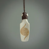 Hand carved engraved bone toki necklace hand made here in New Zealand. One only artistic toki pendant with hand plaited dark brown adjustable cord. Shipped to you with Express Courier. Stand out toki pendant for men and women. Bone Toki with engraved spiral on the back and paua shell insert on the front.