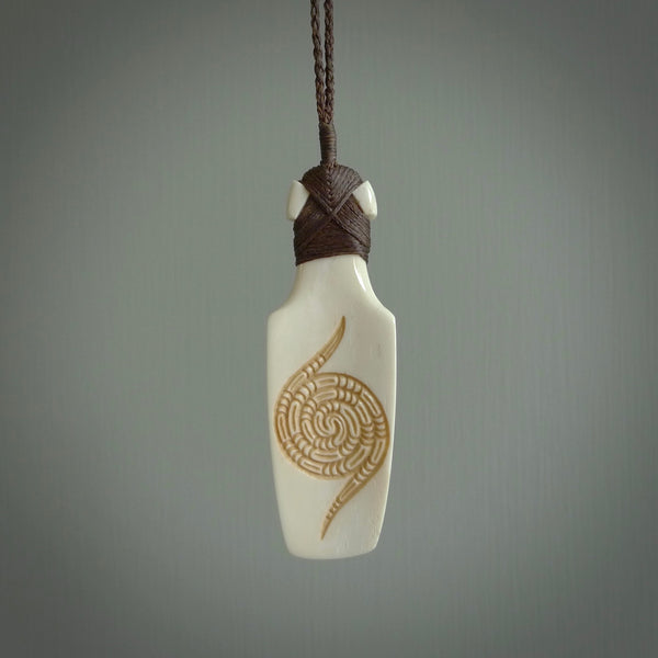 Hand carved engraved bone toki necklace hand made here in New Zealand. One only artistic toki pendant with hand plaited dark brown adjustable cord. Shipped to you with Express Courier. Stand out toki pendant for men and women. Bone Toki with engraved spiral on the back and paua shell insert on the front.