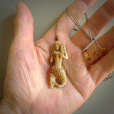This photo shows a photo of a mermaid pendant. It is handcarved from a beautifully creamy piece of woolly mammoth tusk. It is suspended on an adjustable cord.This photo shows a photo of a mermaid pendant. It is handcarved from a beautifully creamy piece of woolly mammoth tusk. It is suspended on an adjustable cord.