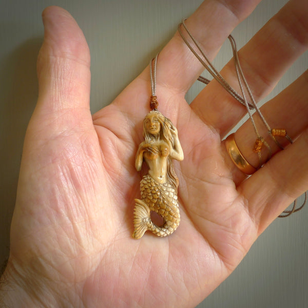 This photo shows a photo of a mermaid pendant. It is handcarved from a beautifully creamy piece of woolly mammoth tusk. It is suspended on an adjustable cord.