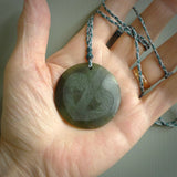 Hand carved jade disc pendant. One side has a double koru etched into the face. This is a subtle and beautiful design. The other side is plain. The cord is a tan colour and is adjustable. The piece was carved for NZ Pacific by Rueben Tipene.