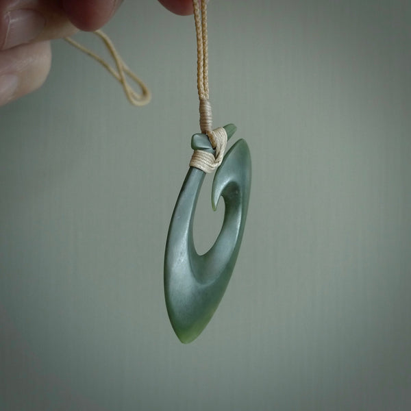 This picture shows a jade hook pendant, also called a hei-matau, carved for us in New Zealand jade. The jade is a wonderful deep mint green pounamu. This is a rare jade loved and valued for its distinctive colour. The carver is Ric Moor - and this is a beautiful example of his work. The cord is a four-plait, adjustable beige coloured necklace.