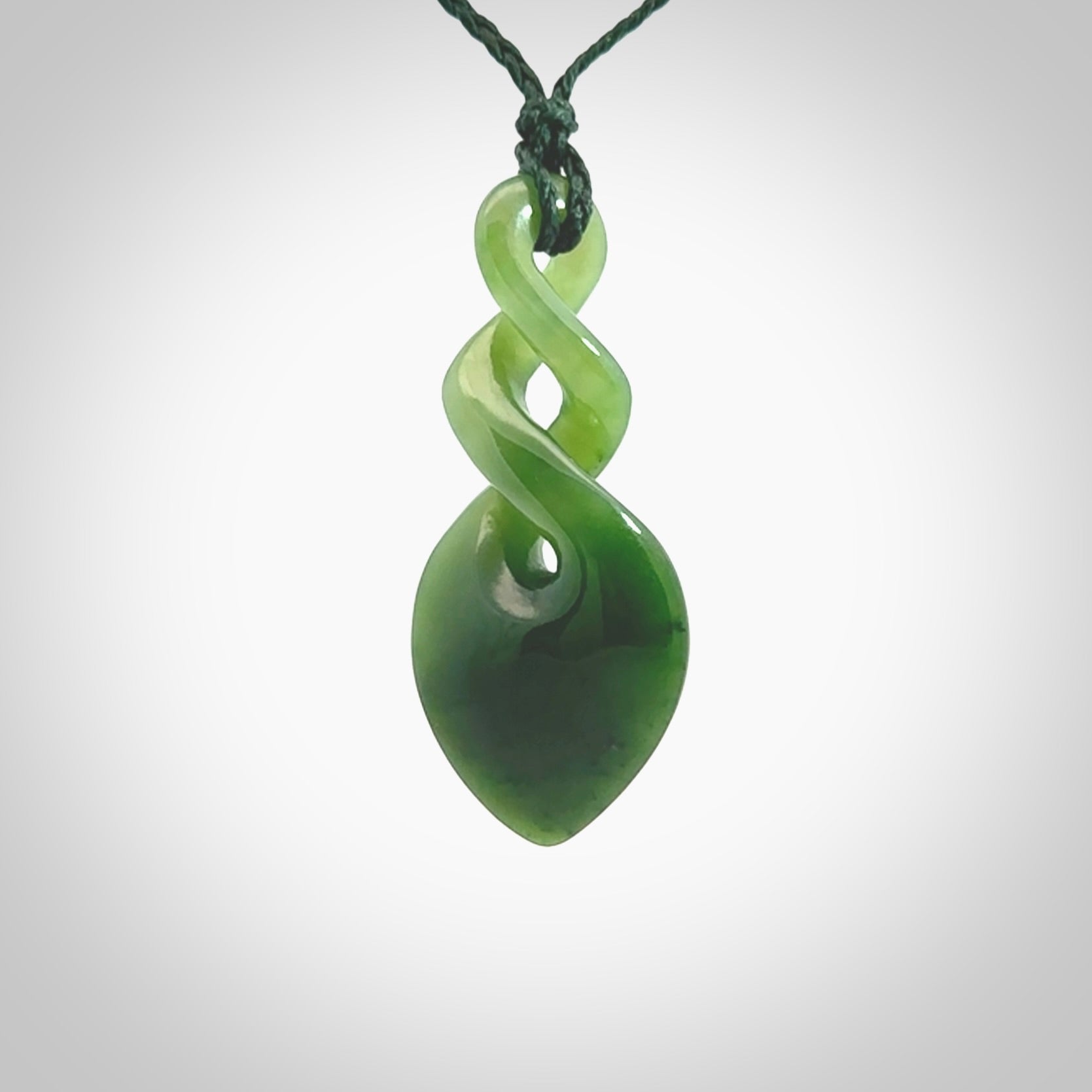 Hand carved New Zealand jade twist pendant. Carved in New Zealand by NZ Pacific. Unique double twist jewellery for sale online. Provided with an adjustable manuka green cord.