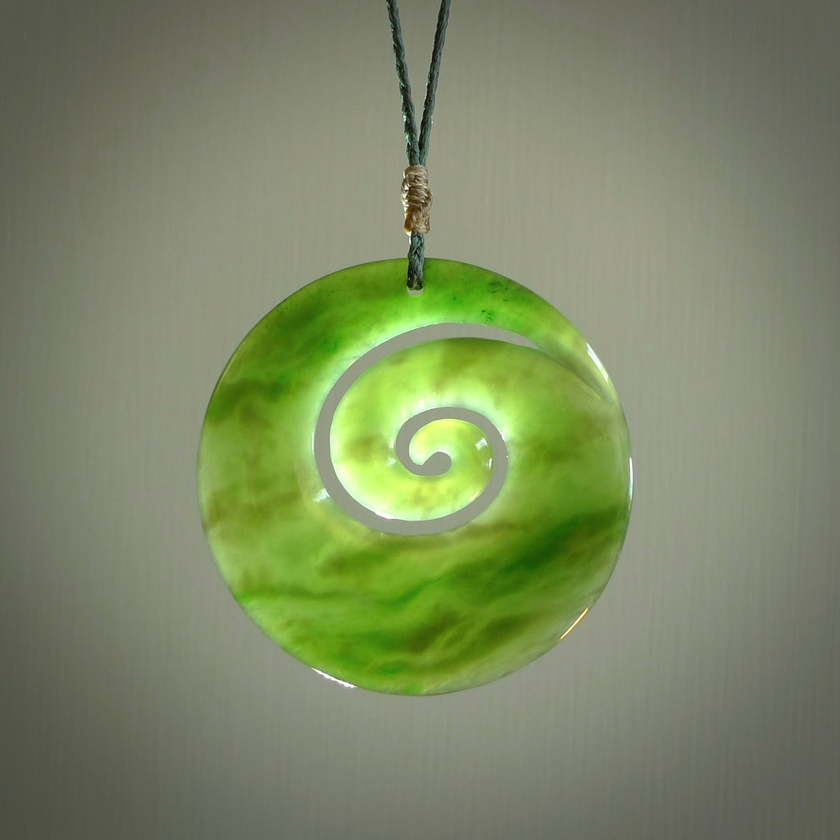 This picture shows a large hand-carved koru. It is carved from British Columbian jade and is suspended from a hand-plaited, black cord. Free delivery worldwide. BC Jade koru necklace.