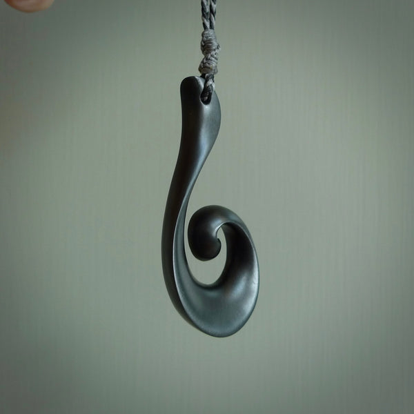 A hand carved large sized Black Jade Koru necklace. The cord is a tan colour and is a fixed length . A large sized hand made hook necklace by New Zealand artist Kerry Thompson. One off work of art to wear.