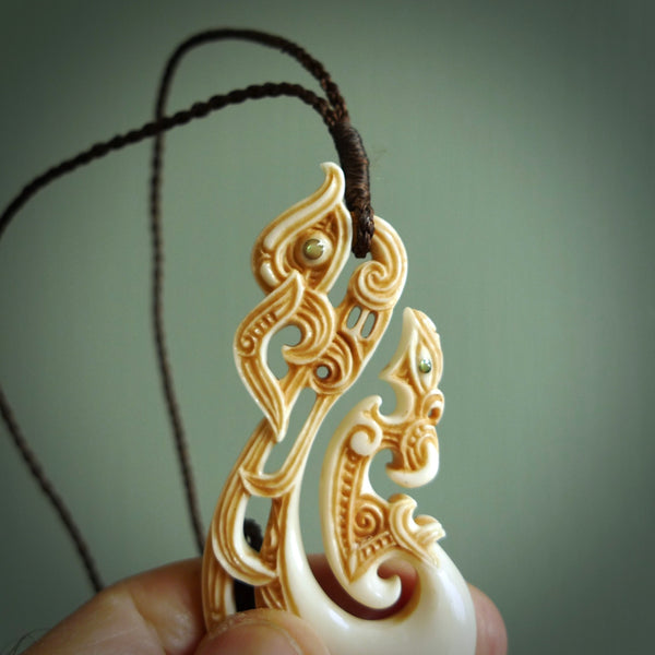 This picture shows a carved manaia in bone. The artist has carved traditional decorative kowhaiwhai designs into the body and these run up the insides of the manaia. These have specific meanings. It is provided with a hand-plaited brown cord that is length adjustable. Free shipping worldwide.