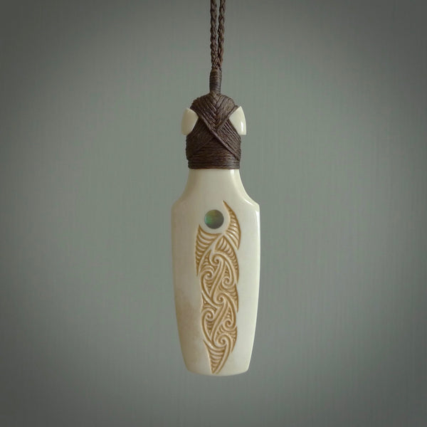 Hand carved engraved bone toki necklace hand made here in New Zealand. One only artistic toki pendant with hand plaited dark brown adjustable cord. Shipped to you with Express Courier. Stand out toki pendant for men and women. Bone Toki with engraved spiral on the back and paua shell insert on the front.