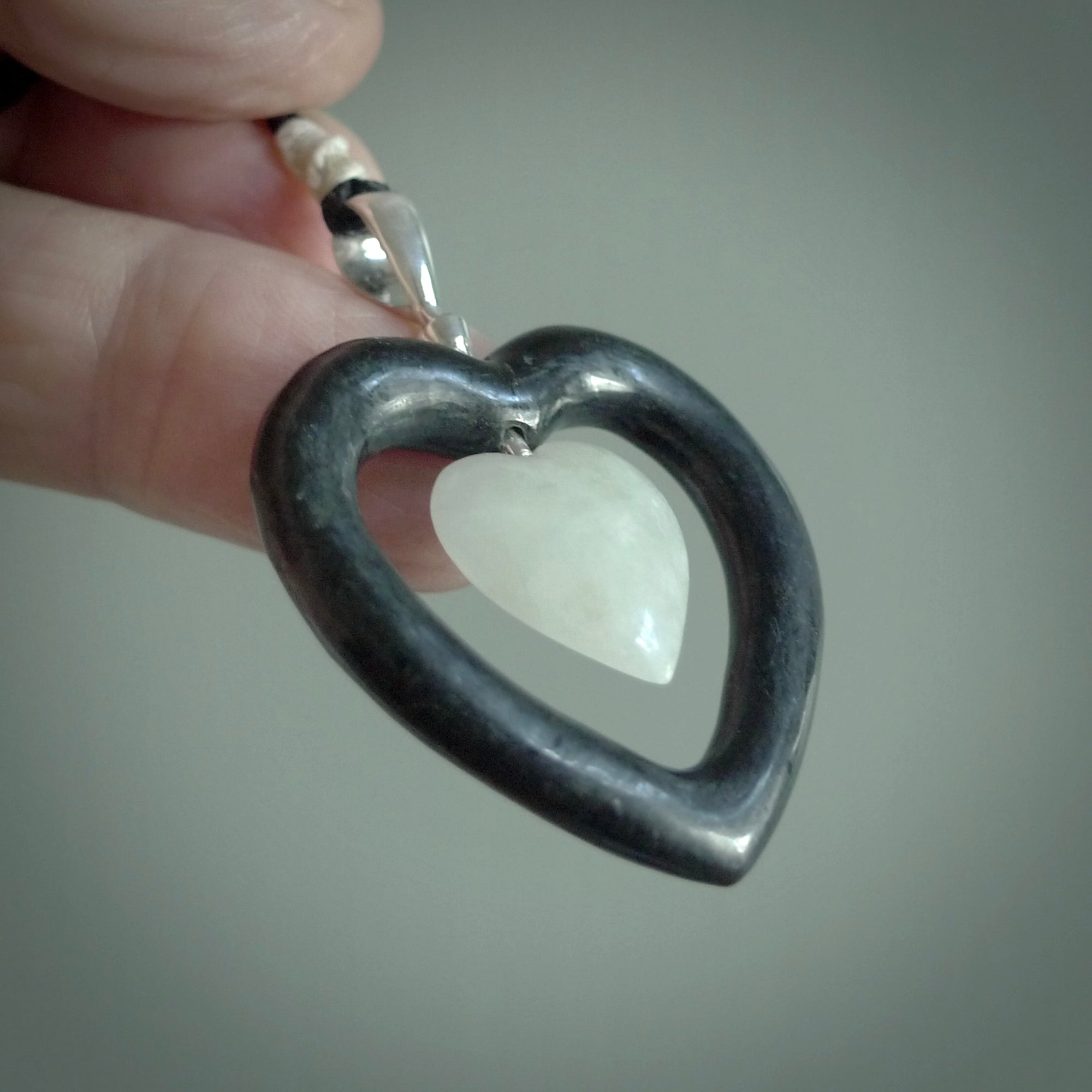Black Jade Heart pendant with Jadeite heart centre. Hand carved for NZ Pacific. Handmade jewellery for sale online. The cord is a 3-braid plait in black and is adjustable. Double heart necklace for men and women. Heart necklace hand made from black jade stone and Jadeite.