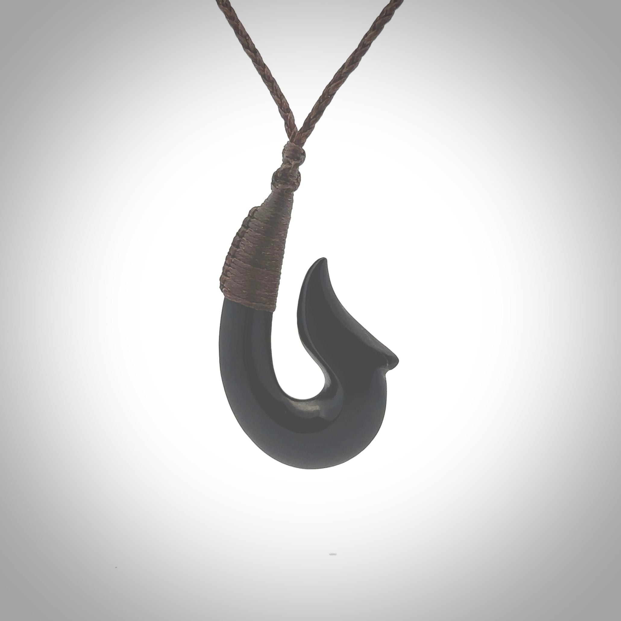 This piece is a hand carved black jade matau pendant, otherwise known as a traditional fish hook necklace. This piece has been carved by us and is made from a wonderful lustrous black jade that we source in Australia. It is a striking traditional piece which we hand bind with a Brown/Flax coloured cord. Delivery is free worldwide.