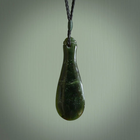 This is a sleek and slender hand carved New Zealand Jade mere pendant. The stone is a very dark green with mottled pale inclusions. The cord is black and adjustable. The pendant has a light polish and just glows.