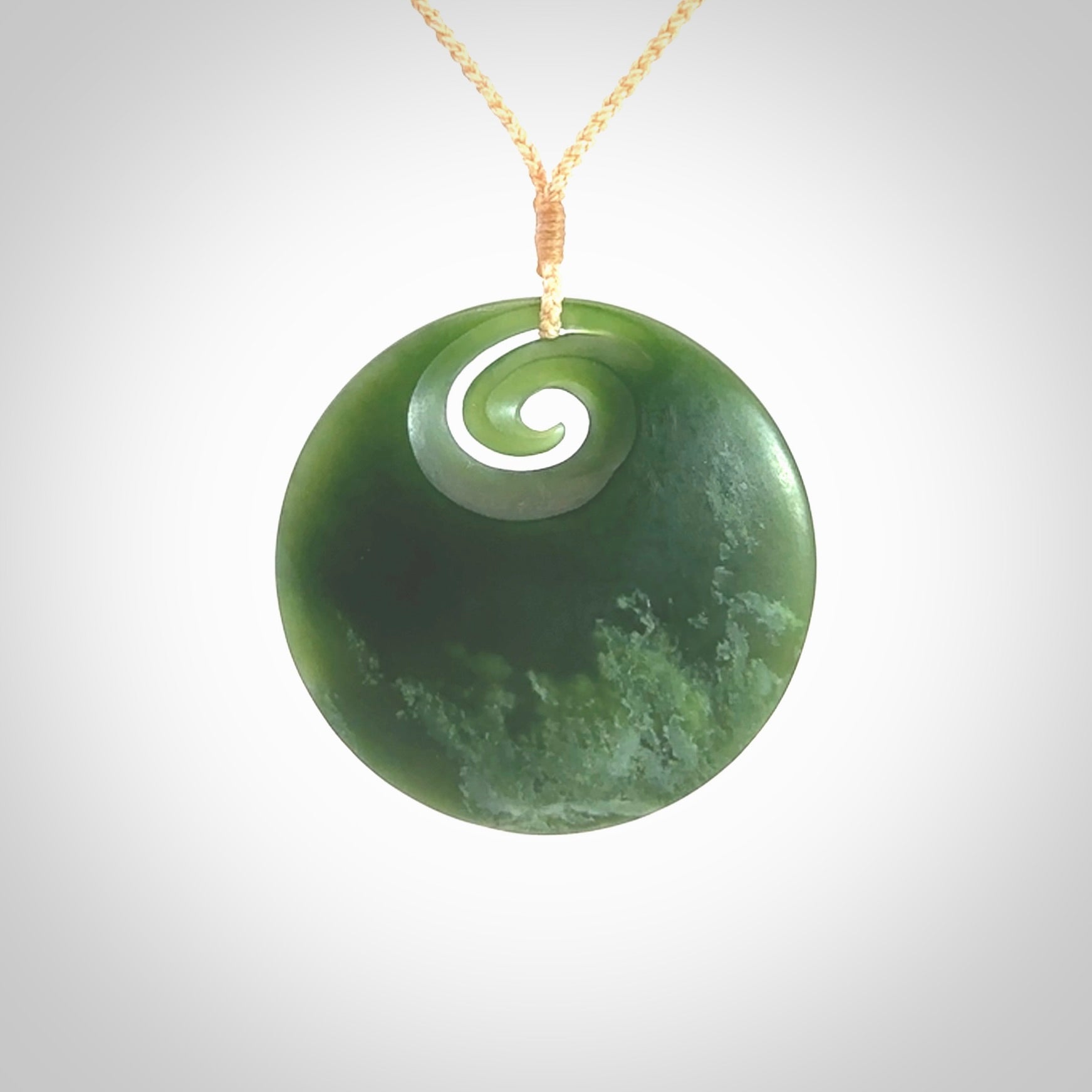 This picture shows a large hand carved jade koru pendant. It is a darker green colour which is quite translucent where the jade is thin. Although a large piece, it is a wonderful, delicate piece of jewellery. The cord is hand plaited and adjustable so that you can position the pendant where it suits you best. This koru was carved for us by Ric Moor. Delivery is free worldwide.