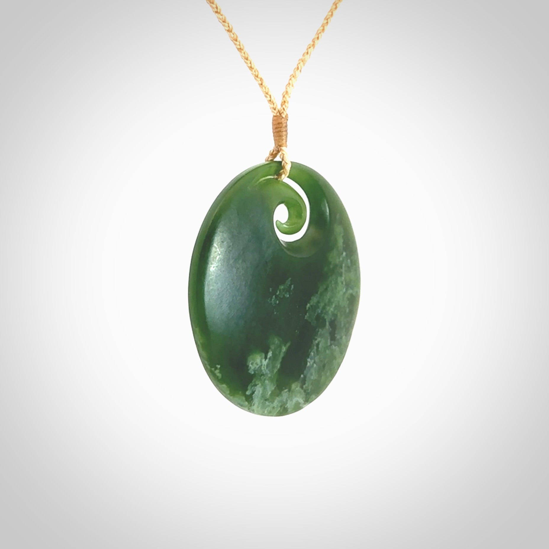This picture shows a large hand carved jade koru pendant. It is a darker green colour which is quite translucent where the jade is thin. Although a large piece, it is a wonderful, delicate piece of jewellery. The cord is hand plaited and adjustable so that you can position the pendant where it suits you best. This koru was carved for us by Ric Moor. Delivery is free worldwide.