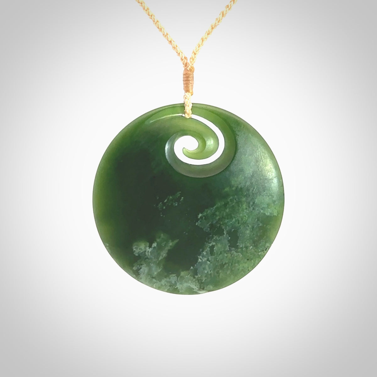 This picture shows a large hand carved jade koru pendant. It is a darker green colour which is quite translucent where the jade is thin. Although a large piece, it is a wonderful, delicate piece of jewellery. The cord is hand plaited and adjustable so that you can position the pendant where it suits you best. This koru was carved for us by Ric Moor. Delivery is free worldwide.