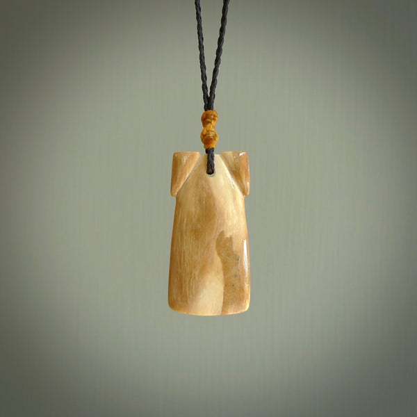 A stunning hand carved Woolly Mammoth Tusk Toki pendant. The toki has a small oval shaped piece of Pāua shell inset into the front face. This piece is bound with an adjustable Black coloured cord. This is a little piece of Art to wear.