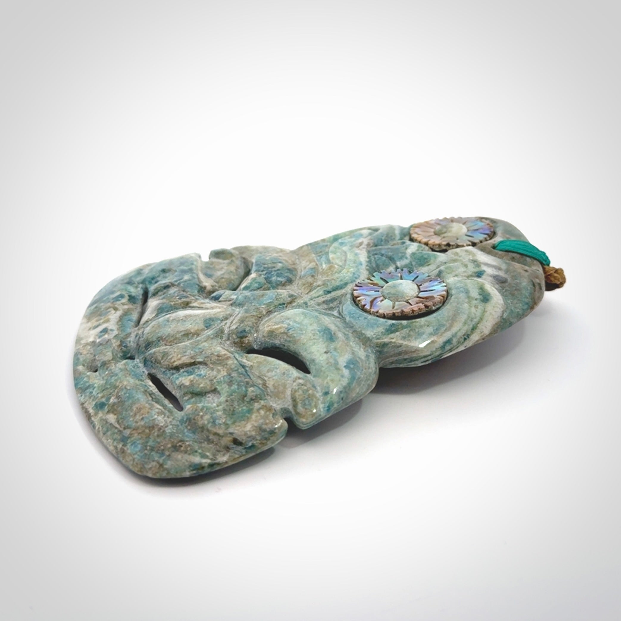 This photo shows a large hand carved Aotea stone Tiki pendant. It is a very light blue colour with pāua shell insert eyes. The cord is a thick camel colour and is length adjustable