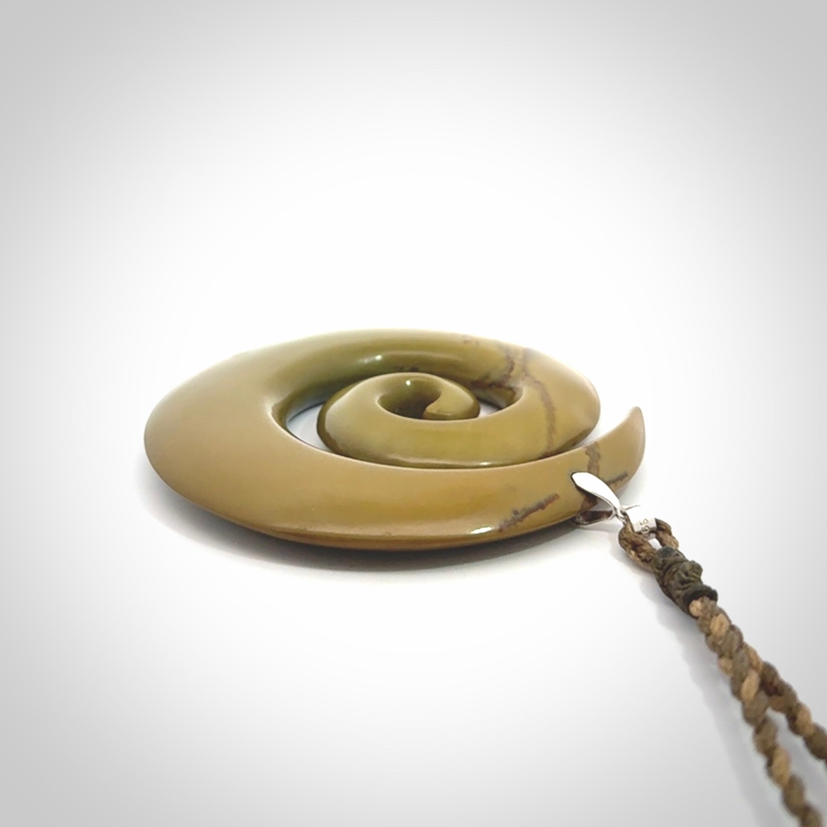 This picture shows a large hand-carved koru. It is carved from New Zealand flower jade and is suspended from an adjustable cord.